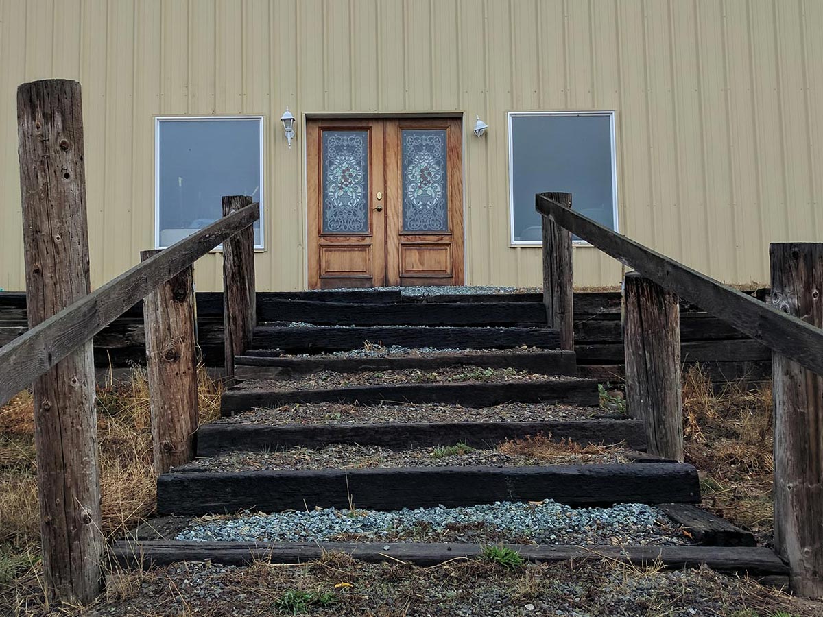 A stairs made of wooden railroad ties leads up to a yellow barn with stained glass doors
